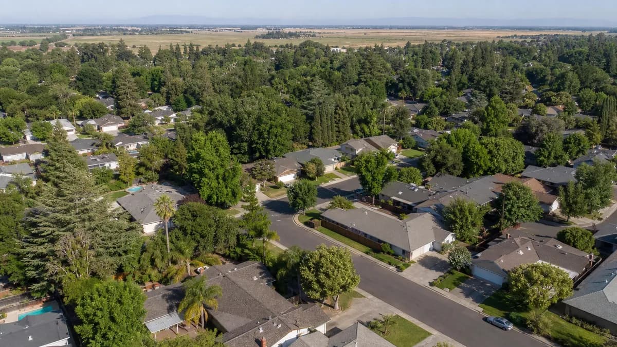 Aerial view of a tree-lined suburban neighborhood of one-story homes with flat valley land beyond.